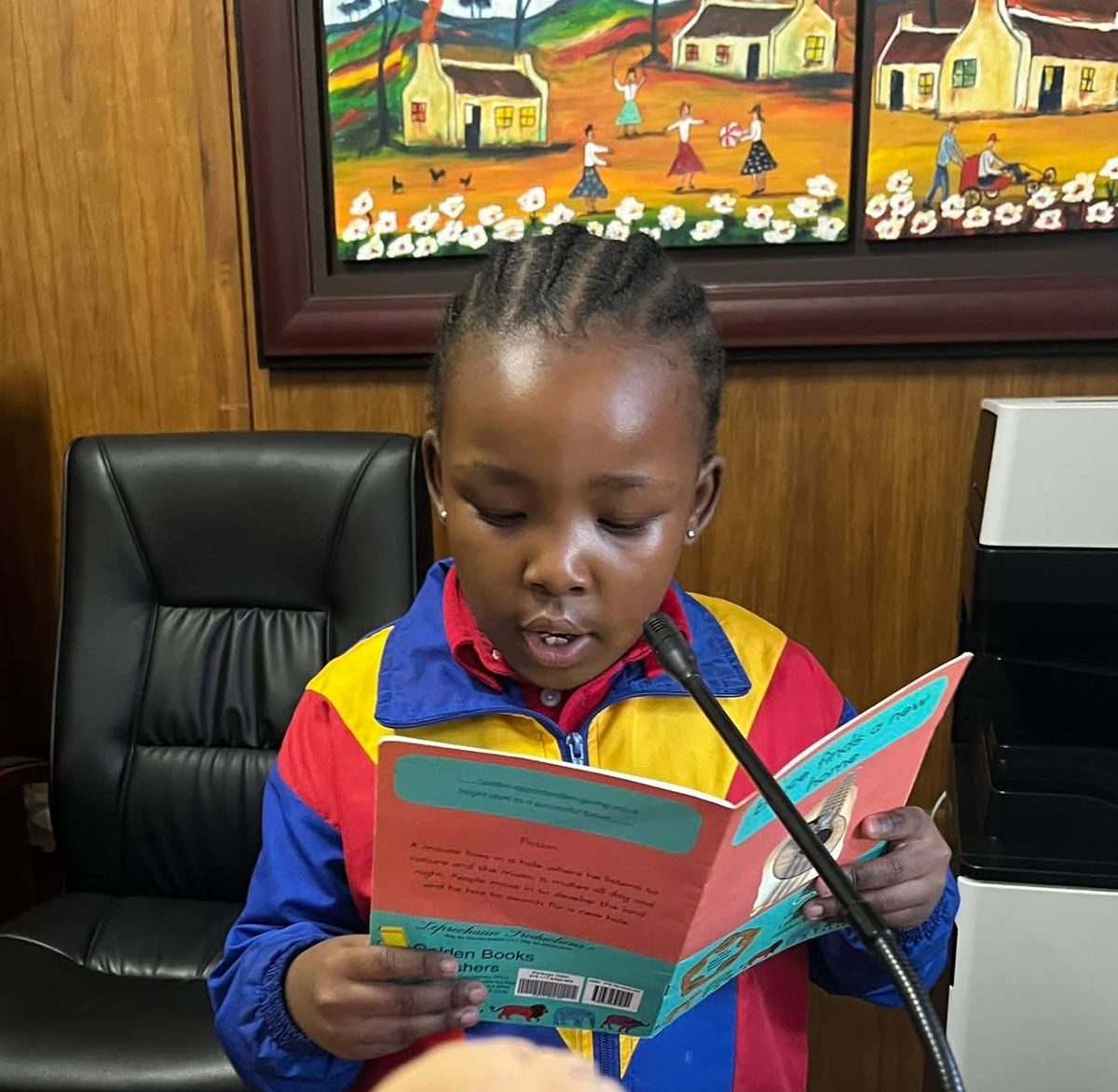 A young Nory reading a storybook aloud at the microphone