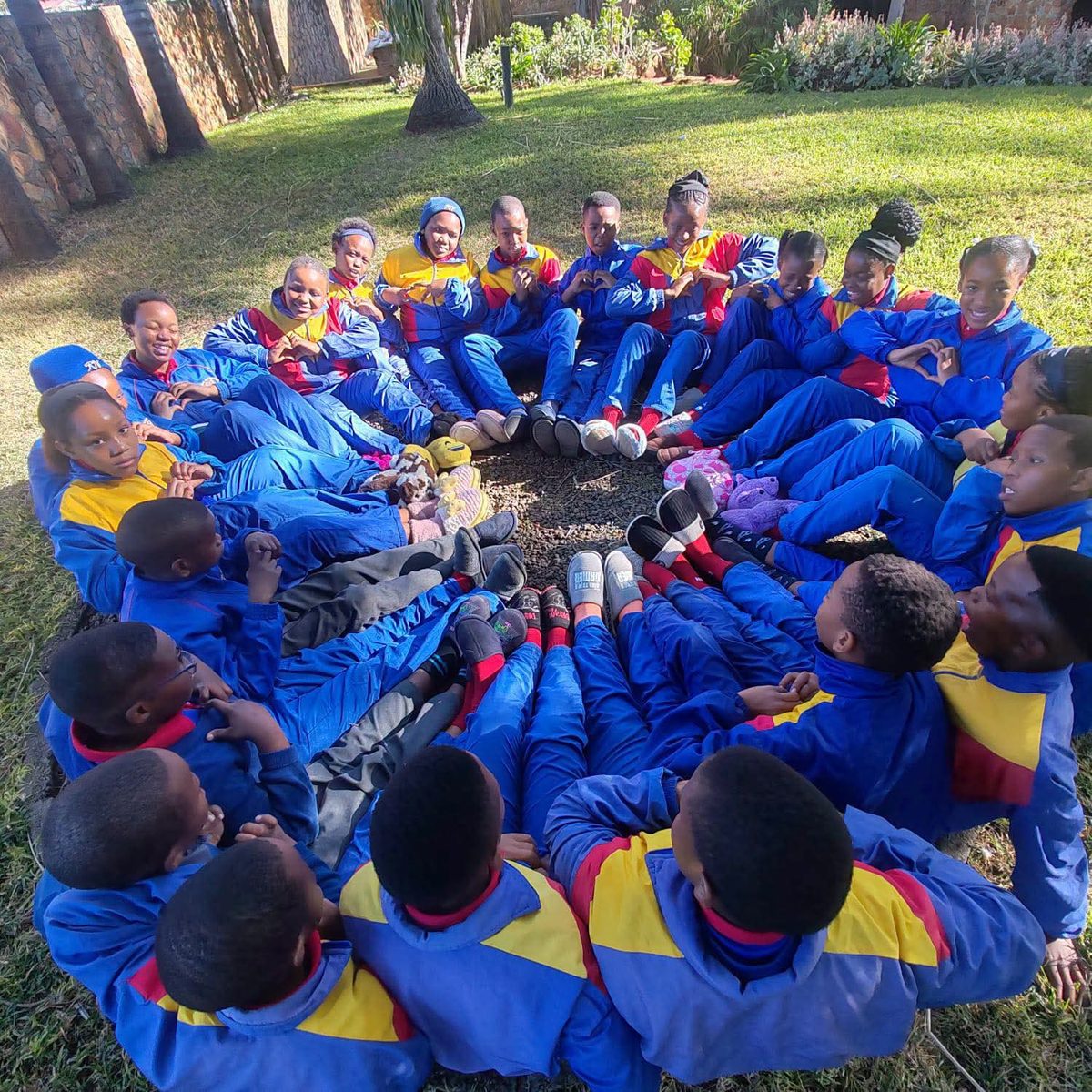 Nories sitting in a circle on the grass, making heart signs with their hands